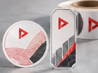 Round and shaped printed labels next to a roll of self-adhesive label material